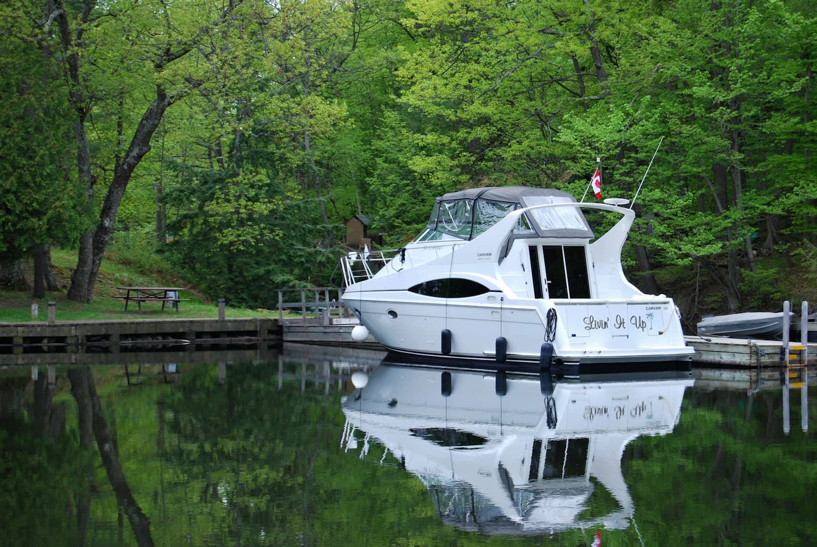 White motor yacht moored at wooden dock with perfect reflection in calm water, surrounded by green trees