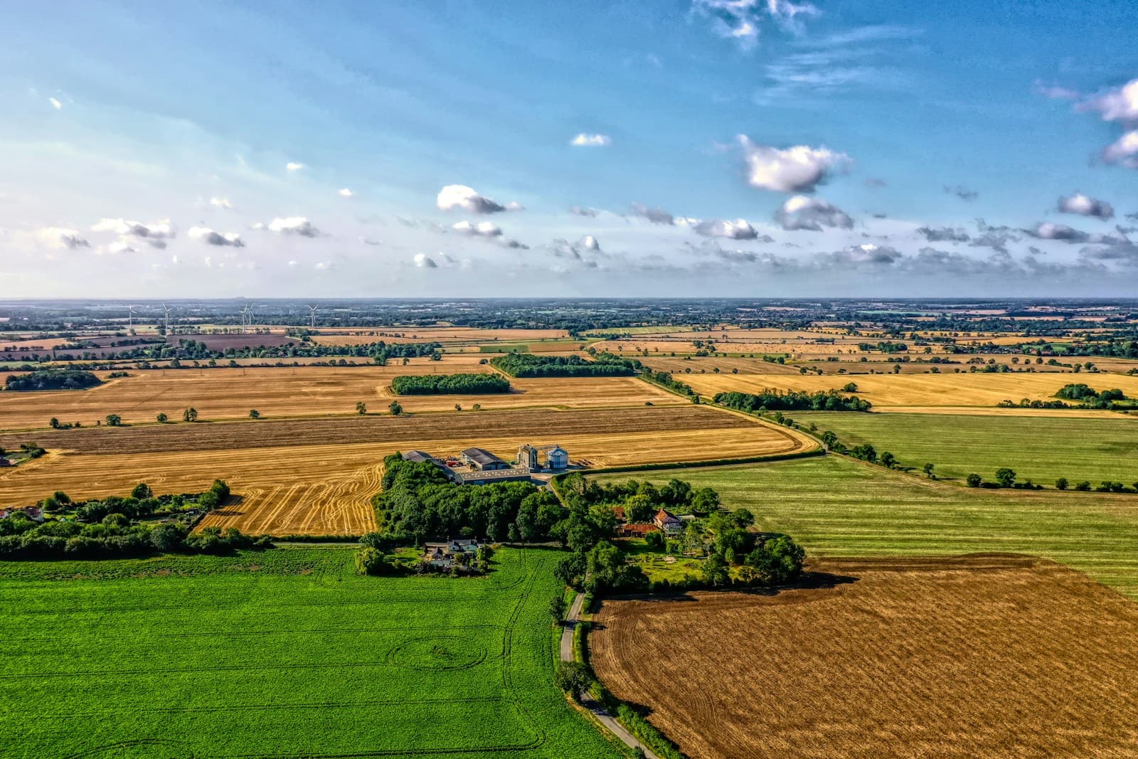 Aerial view of rural farmland with green and brown agricultural fields under blue sky with clouds