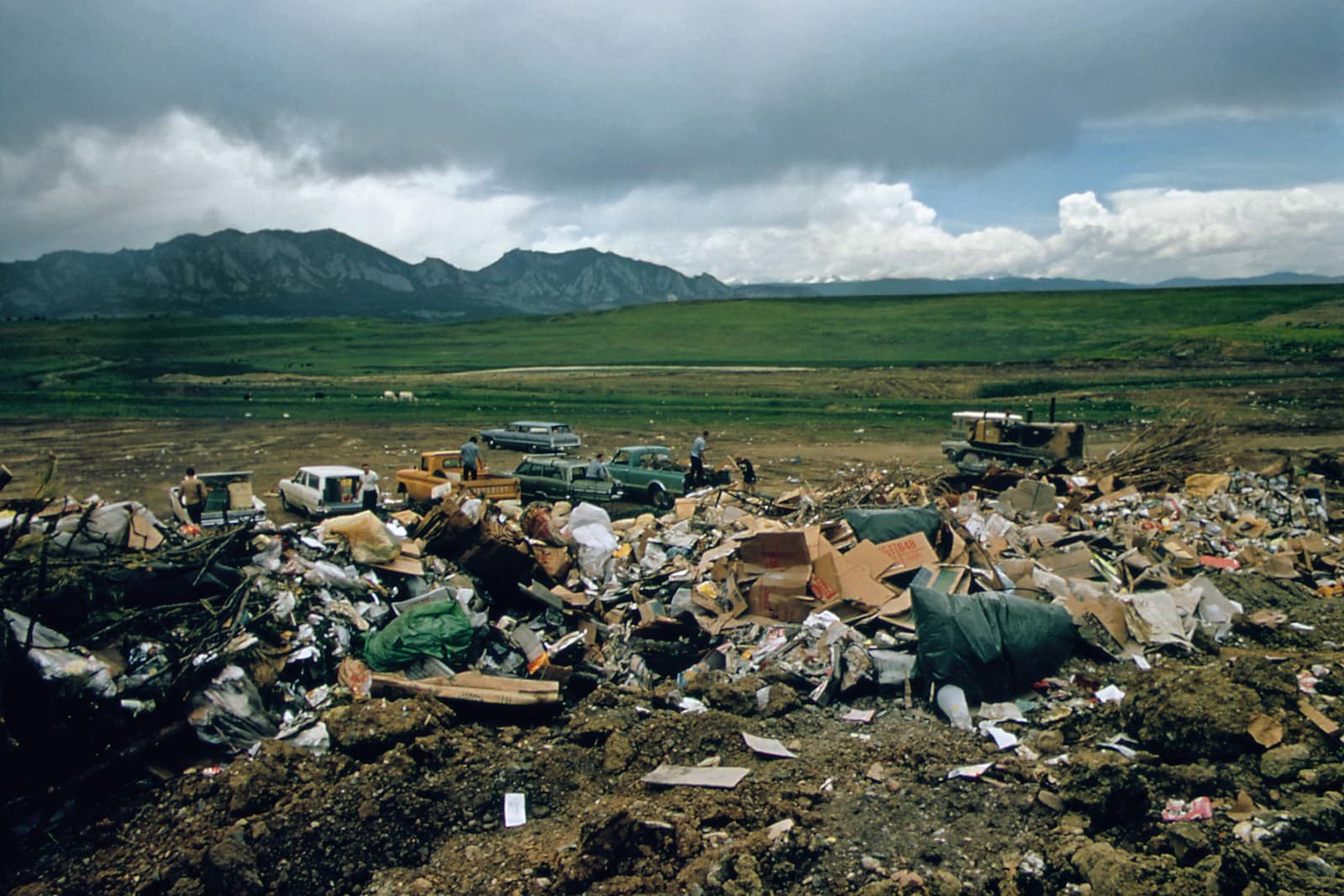Large pile of scattered trash and debris in remote landscape with mountains and cloudy sky in background