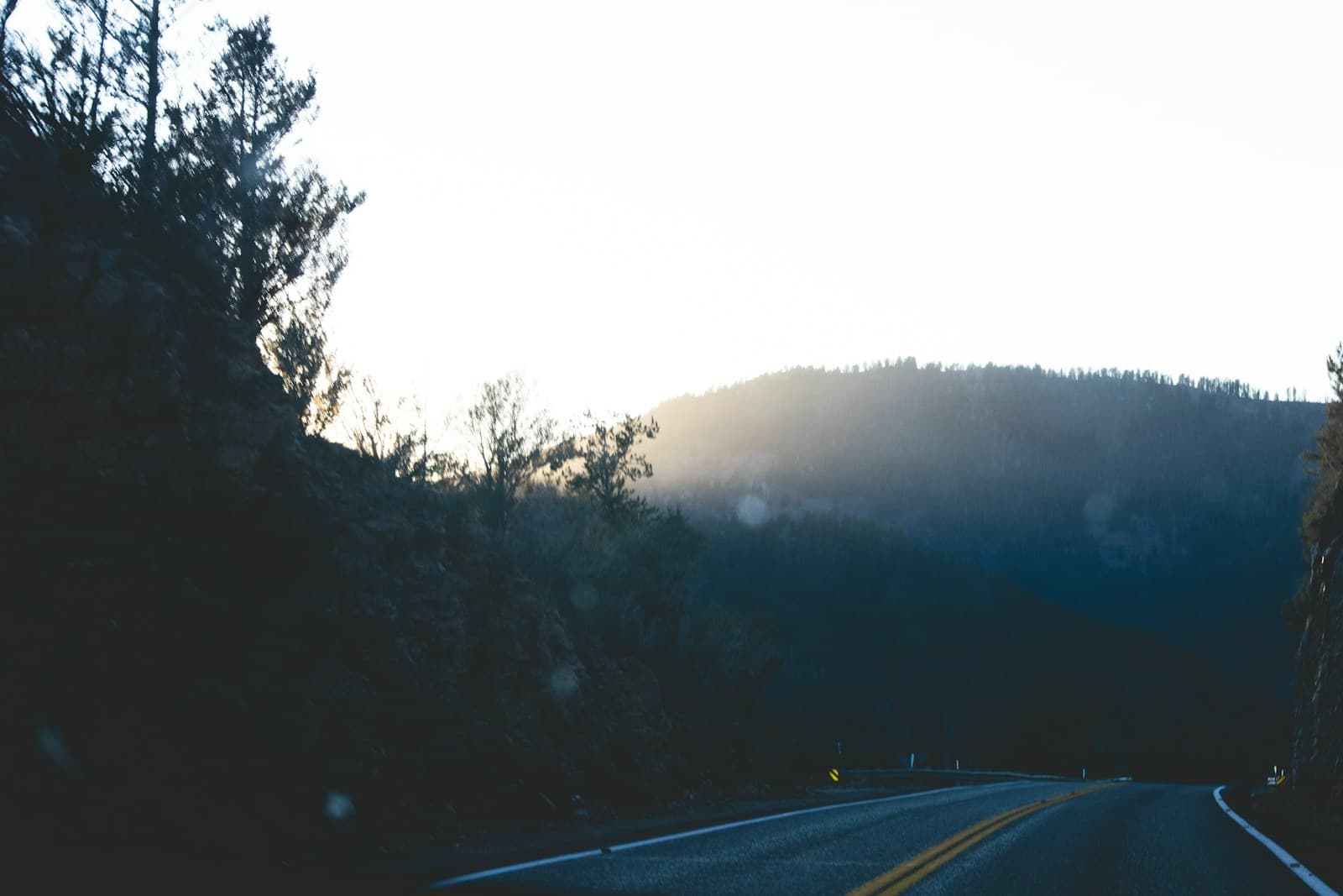 Winding mountain road with sunlight glowing behind forested hills
