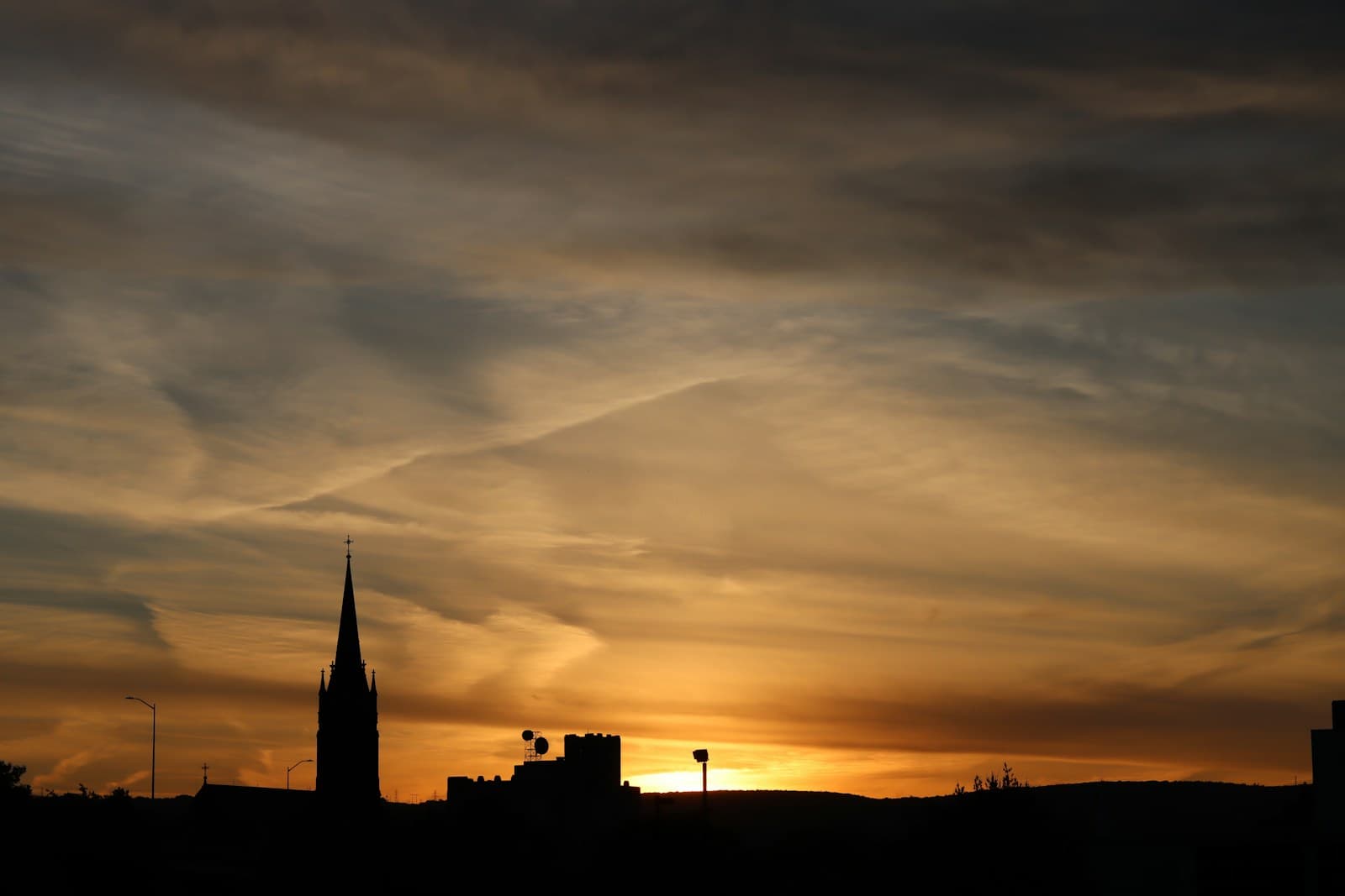 City skyline silhouette with church spire against dramatic orange sunset sky with clouds