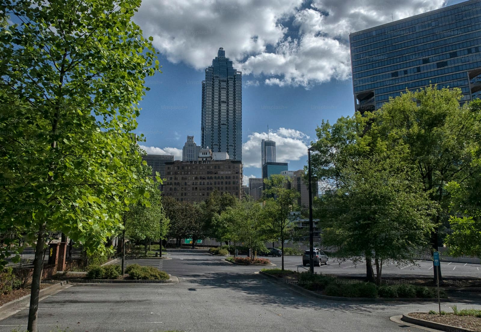 Urban park walkway with trees leading to city skyline with tall buildings under cloudy blue sky