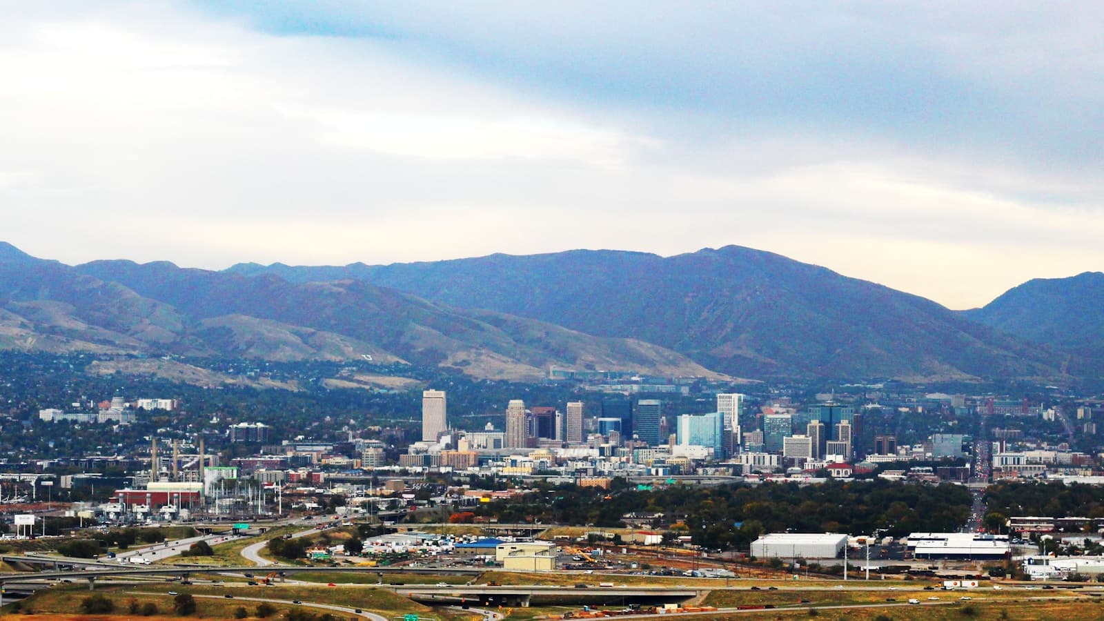 City skyline with downtown buildings and mountains in background under cloudy sky