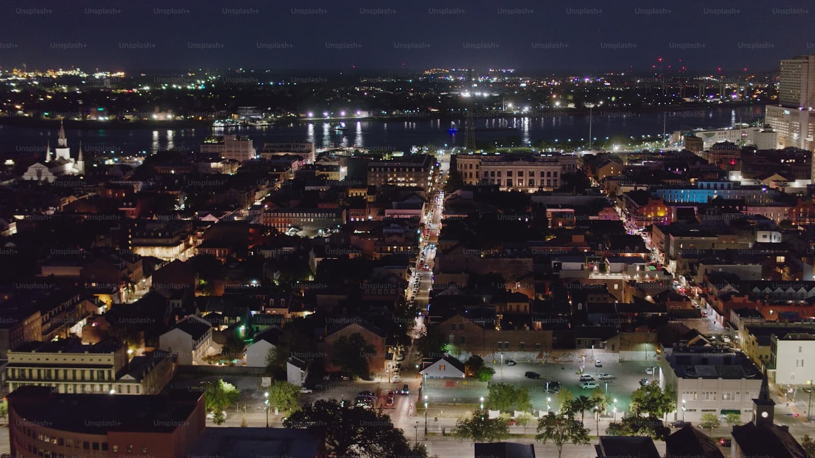Aerial night view of a city with lit streets in grid pattern, historic buildings, and large body of water in background