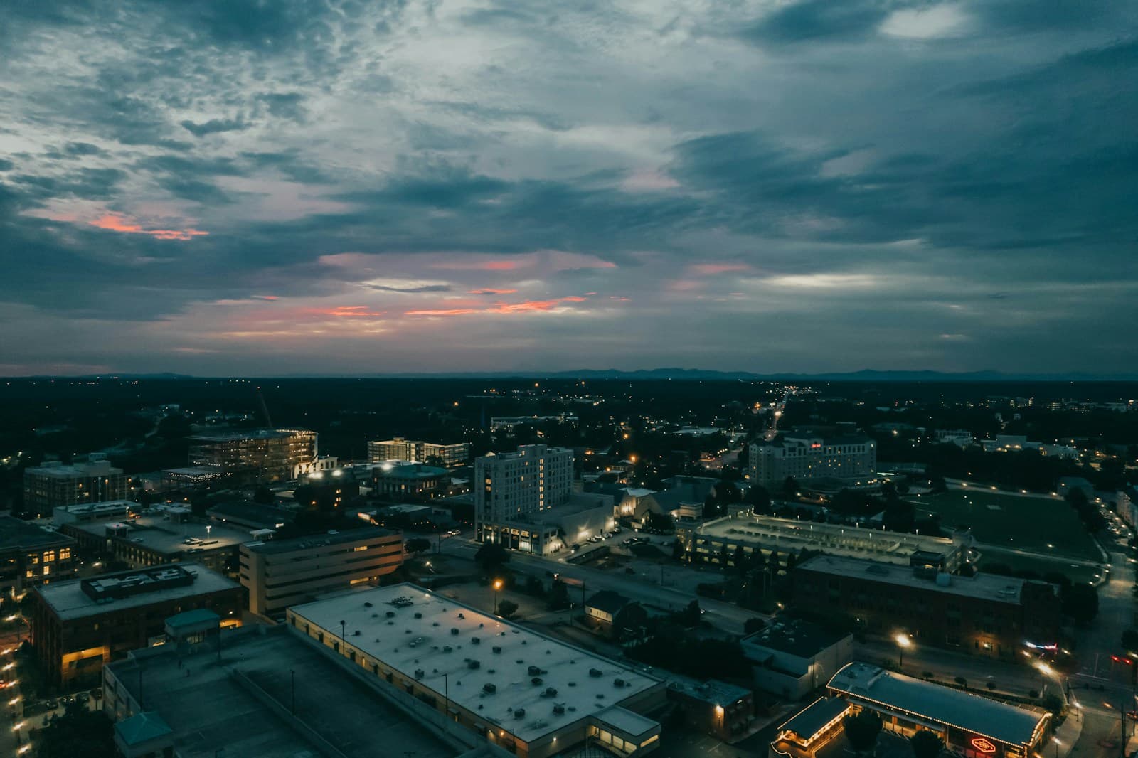 Aerial view of city at twilight with dramatic cloudy sky and urban buildings lit by evening lights