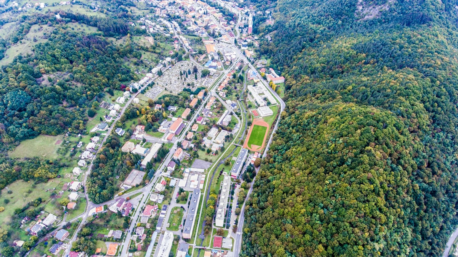 Aerial view of a small town in a forested mountain valley with buildings and roads surrounded by dense green hills
