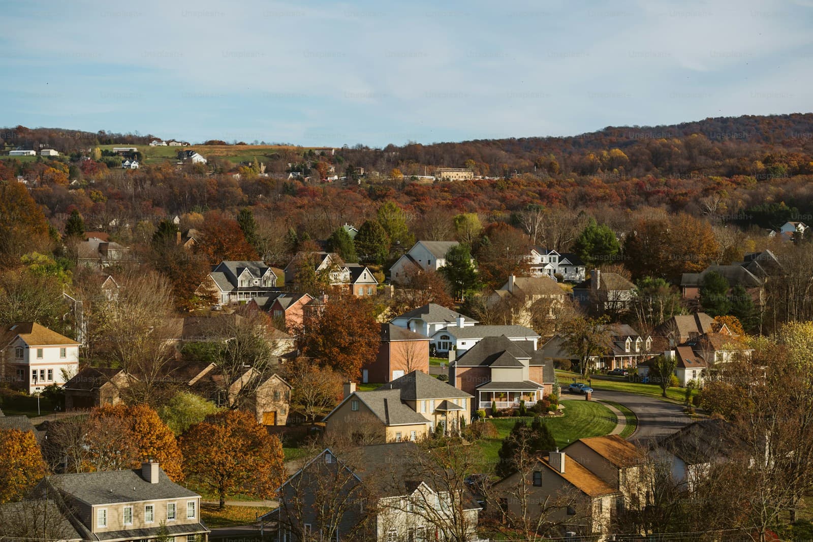 Aerial view of suburban neighborhood with houses among colorful autumn trees and rolling hills