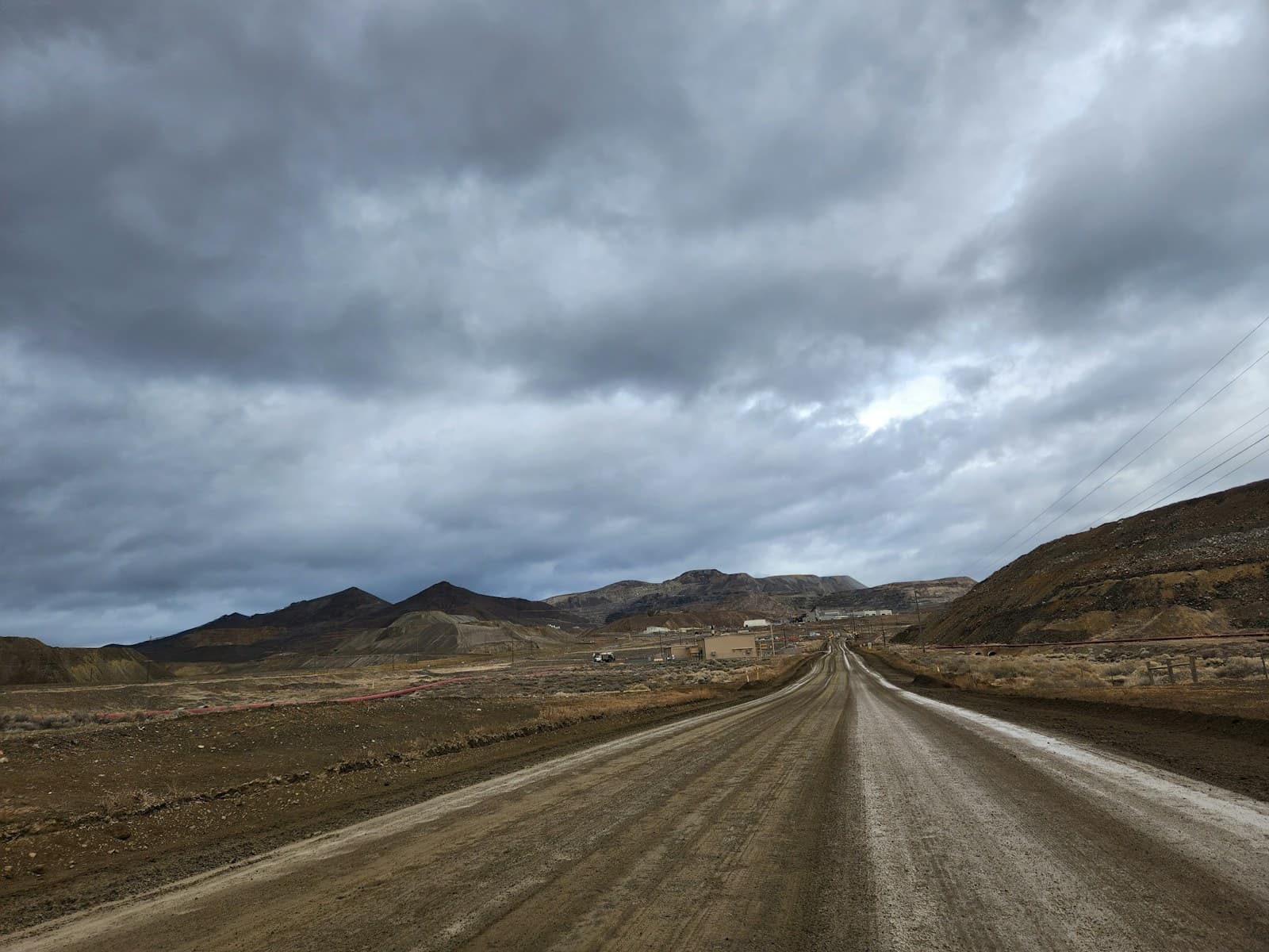 Empty dirt road stretching through desert landscape with mountains and stormy gray clouds overhead